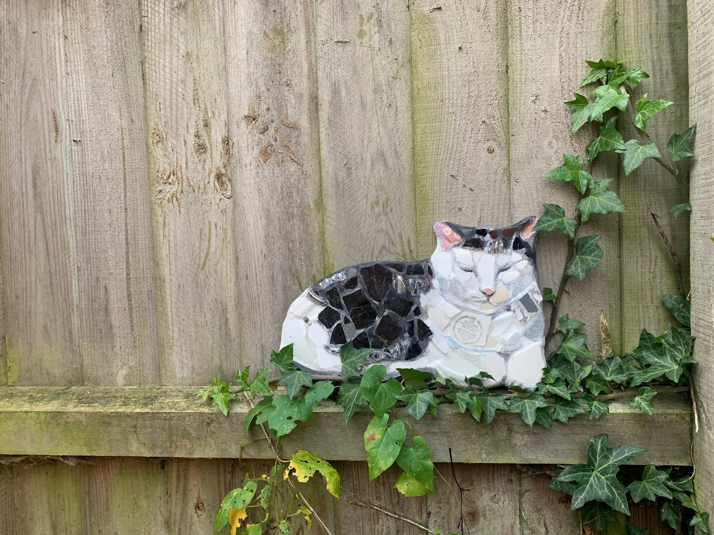 Mosaic cat resting on a fence amongst ivy