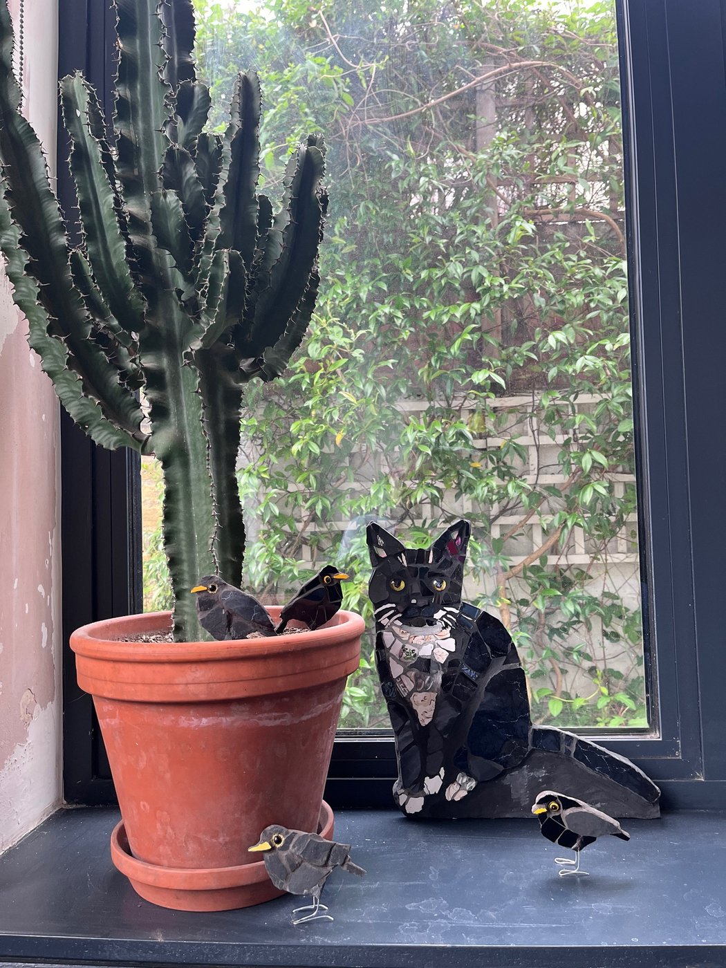 Mosaic black cat on a windowsill with mosaic blackbirds