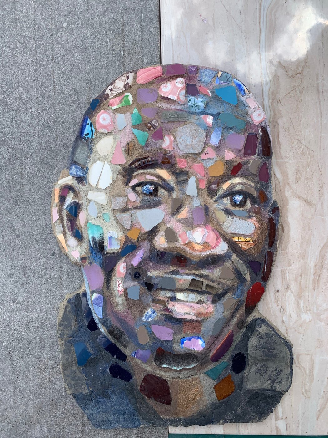 Mosaic portrait of a man, made from small ceramic, glass and tile shards in pink, blue, purple and warm earth tones