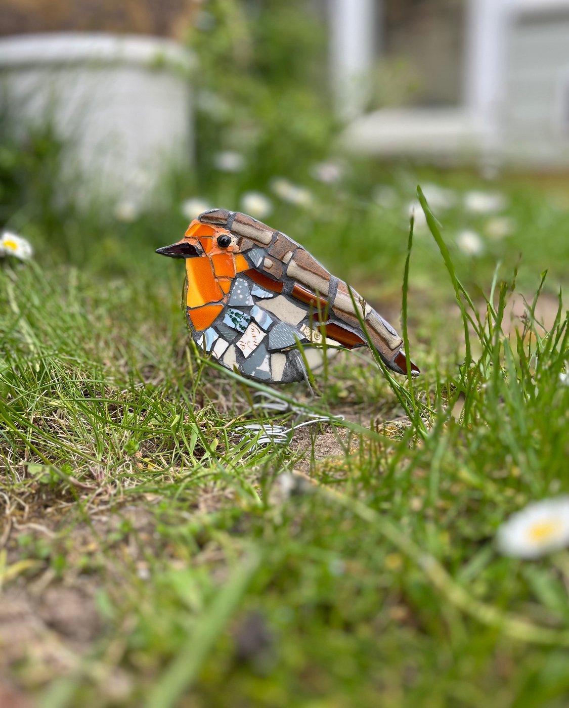 Small mosaic robin standing in grass with daisies