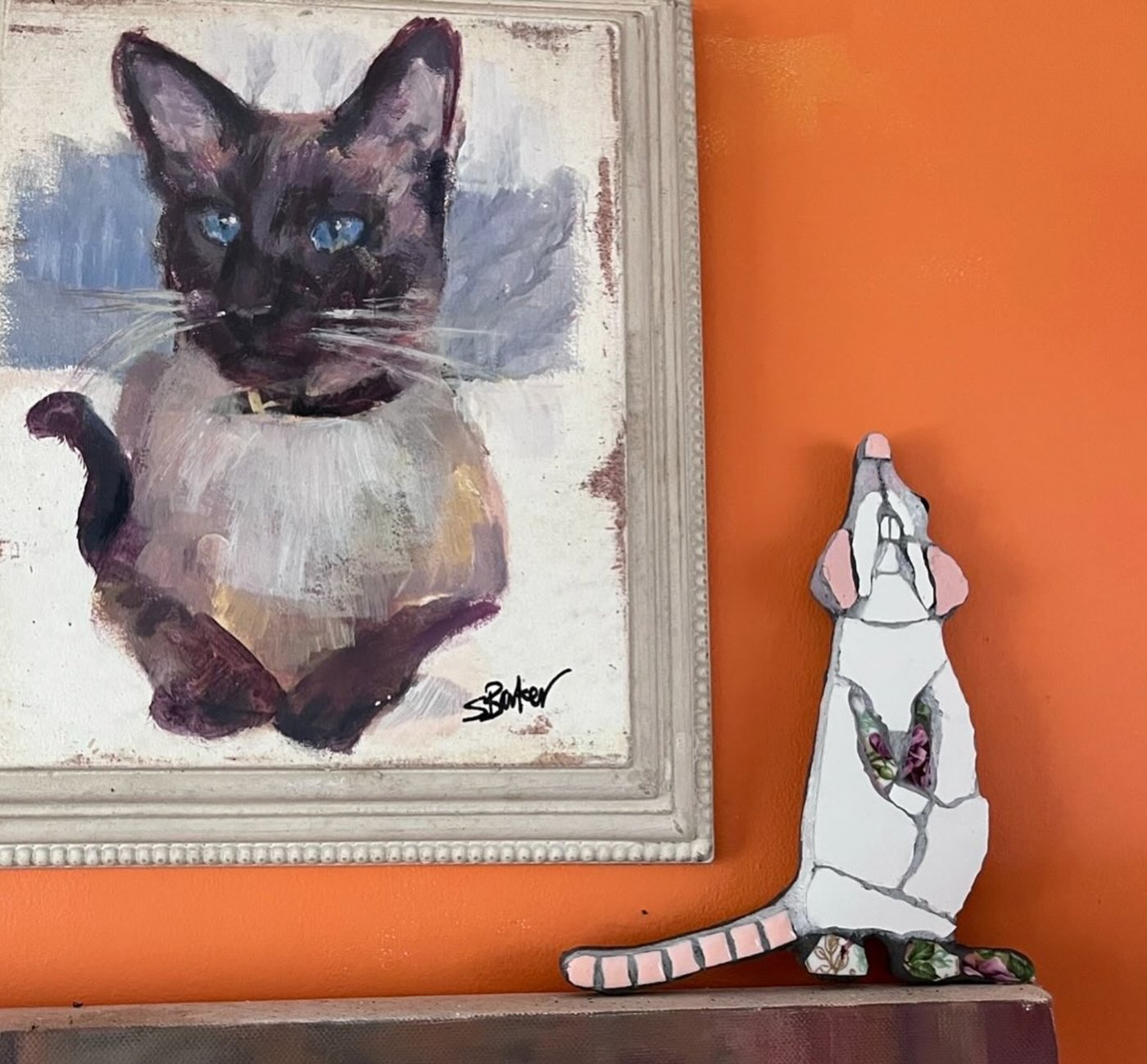 Mosaic standing rat next to an oil painting of a Siamese cat