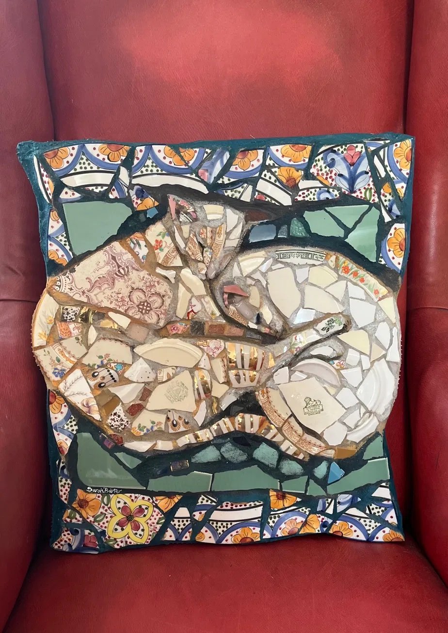Mosaic of a sleeping cat made from vintage china in soft creams, pinks and greens